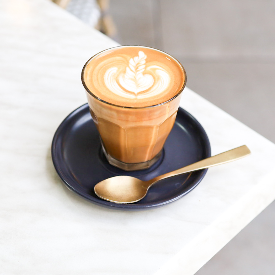 Latte with feather art in a glass on a navy saucer
