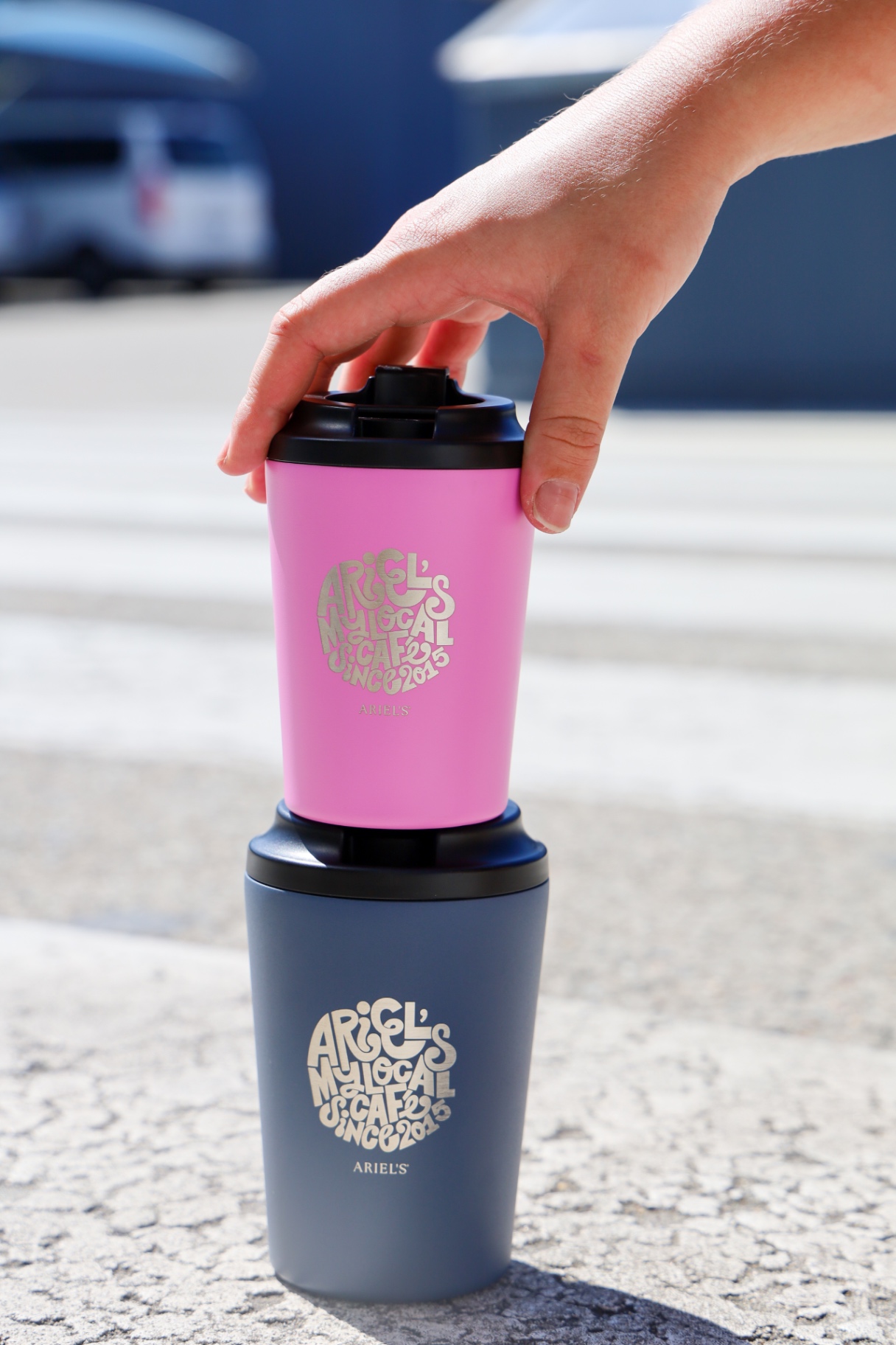 Pink and navy Ariel's reusable keep cups stacked on the pavement