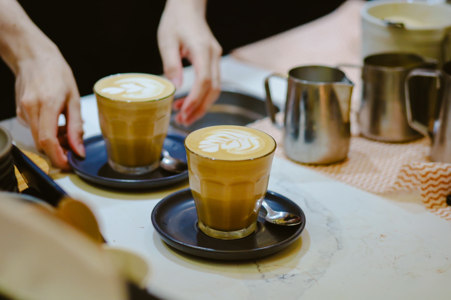 Two lattes with feather latte art served on dark saucers